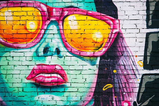 Farebná ženská tvár s okuliarmi namaľovaná na tehlovej stene.jpg
